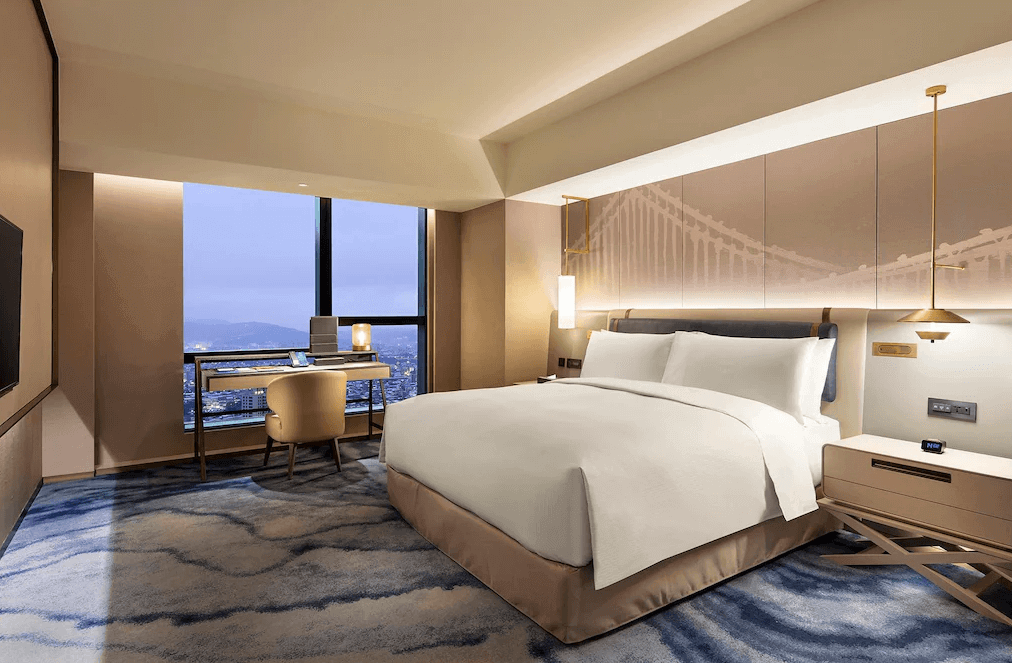 【板橋住宿】台北新板希爾頓酒店 現代化客房，設有大床、大片落地窗可遠眺市景，搭配舒適書桌與暖色系燈光設計，營造優雅住宿氛圍。