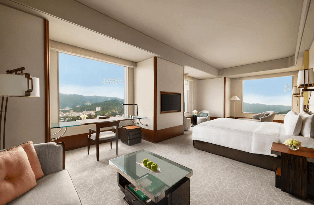 【大安住宿】"大安住宿精選示意圖"台北遠東香格里拉客房景觀 —— 寬敞的雙人房，大片窗戶可欣賞山景，內有舒適沙發、書桌與玻璃茶几，採光明亮。