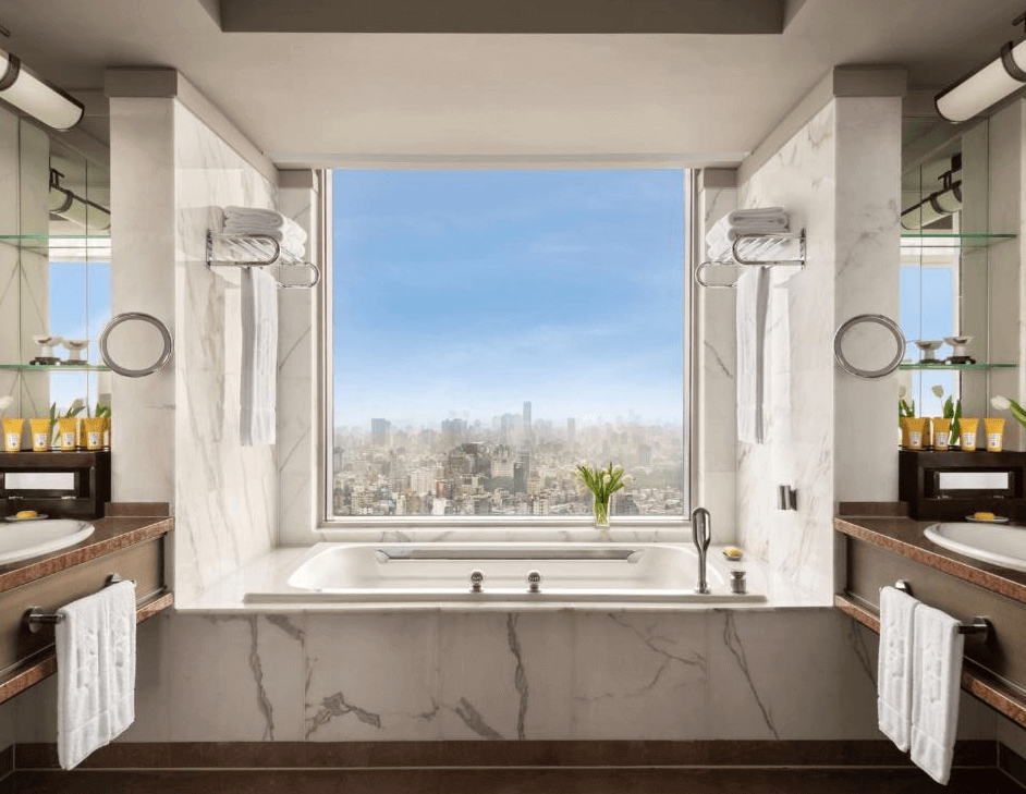 【大安住宿】台北遠東香格里拉浴室 —— 大理石裝潢浴室，中央設有景觀浴缸，窗外俯瞰整個台北市區景色，兩側各有洗手台與盥洗備品。