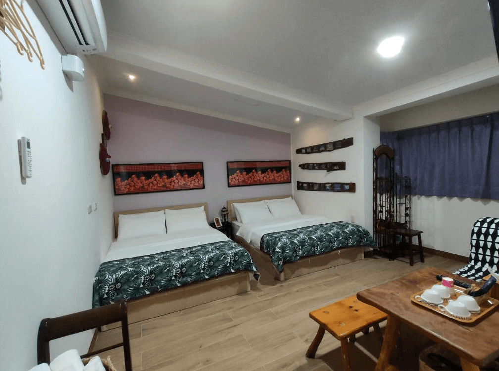 【太麻里住宿】吉廬夫敢藝文民宿四人房，兩張雙人床搭配綠色花葉床單，牆上掛有排灣族藝術裝飾，房內設有木桌與茶具。