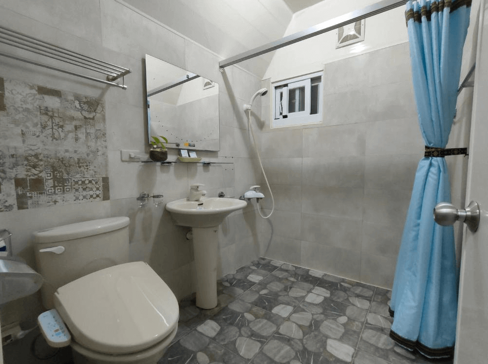 【太麻里住宿】吉廬夫敢藝文民宿浴室，乾濕分離設計，牆面以灰白色磁磚搭配石紋地板，設有洗手台、馬桶與藍色浴簾。