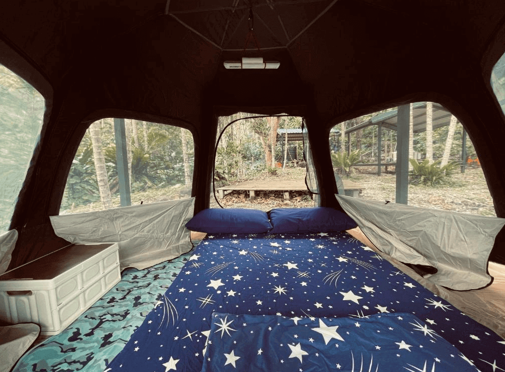 【蘭嶼住宿】吉米探險家露營地&潛水俱樂部帳篷內部：帳篷內鋪設星空圖案床墊與藍色枕頭，四周有透明窗戶可欣賞戶外綠意，營造舒適的露營氛圍。