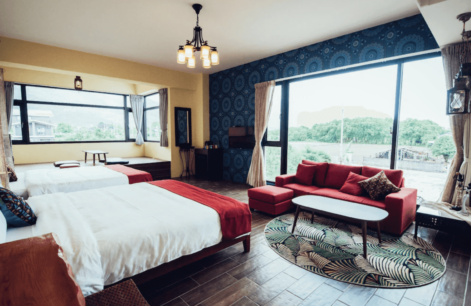 【吉安住宿】哉煙煙民宿雙人房，設有大片落地窗與鄉村景觀，室內搭配紅色沙發、木質地板與藍色牆面裝飾，採光充足、視野遼闊。