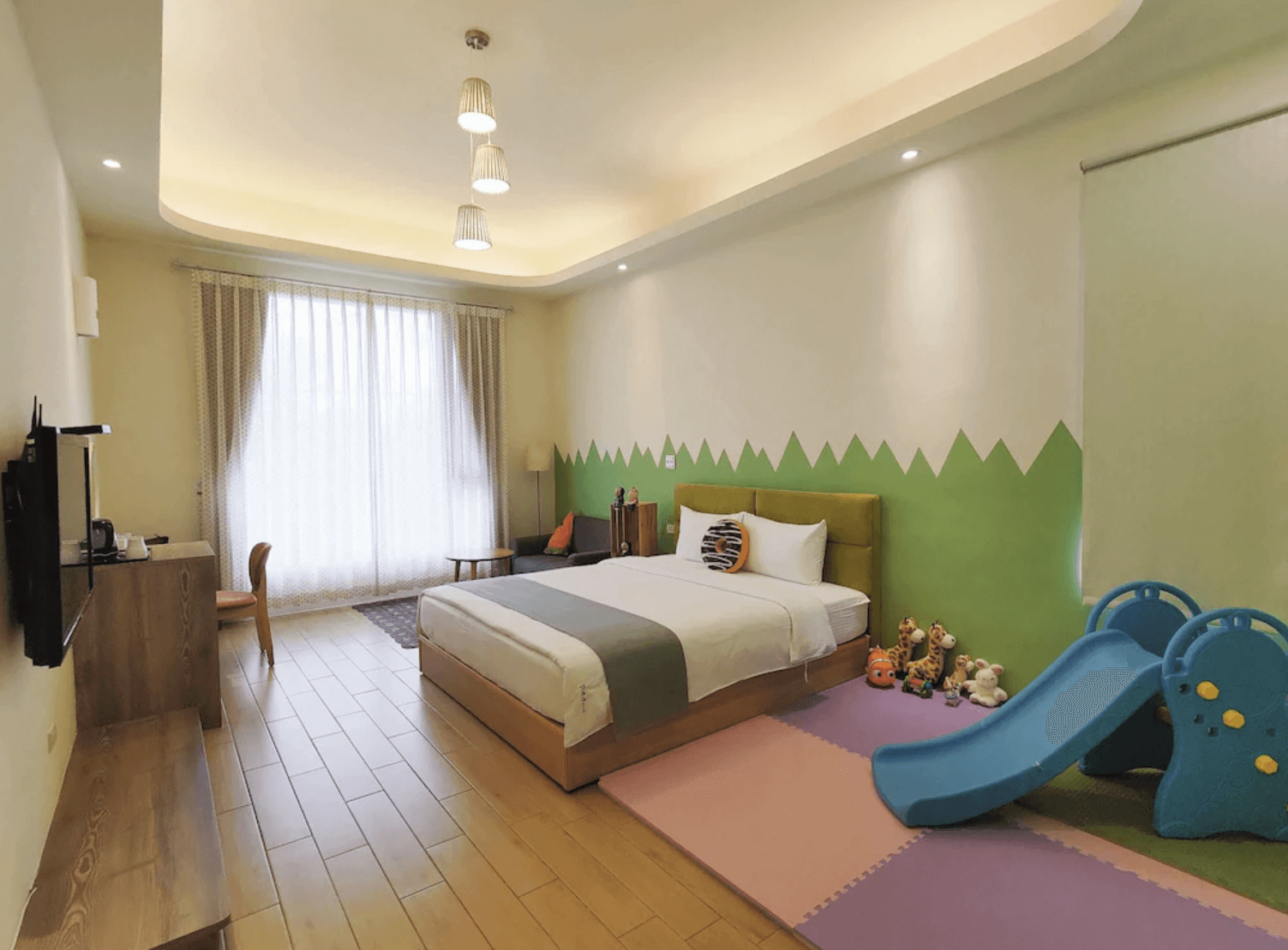 【吉安住宿】哉煙煙民宿親子主題房，房內有單張雙人床、綠色草地造型牆面、遊戲滑梯與地墊，適合親子入住。