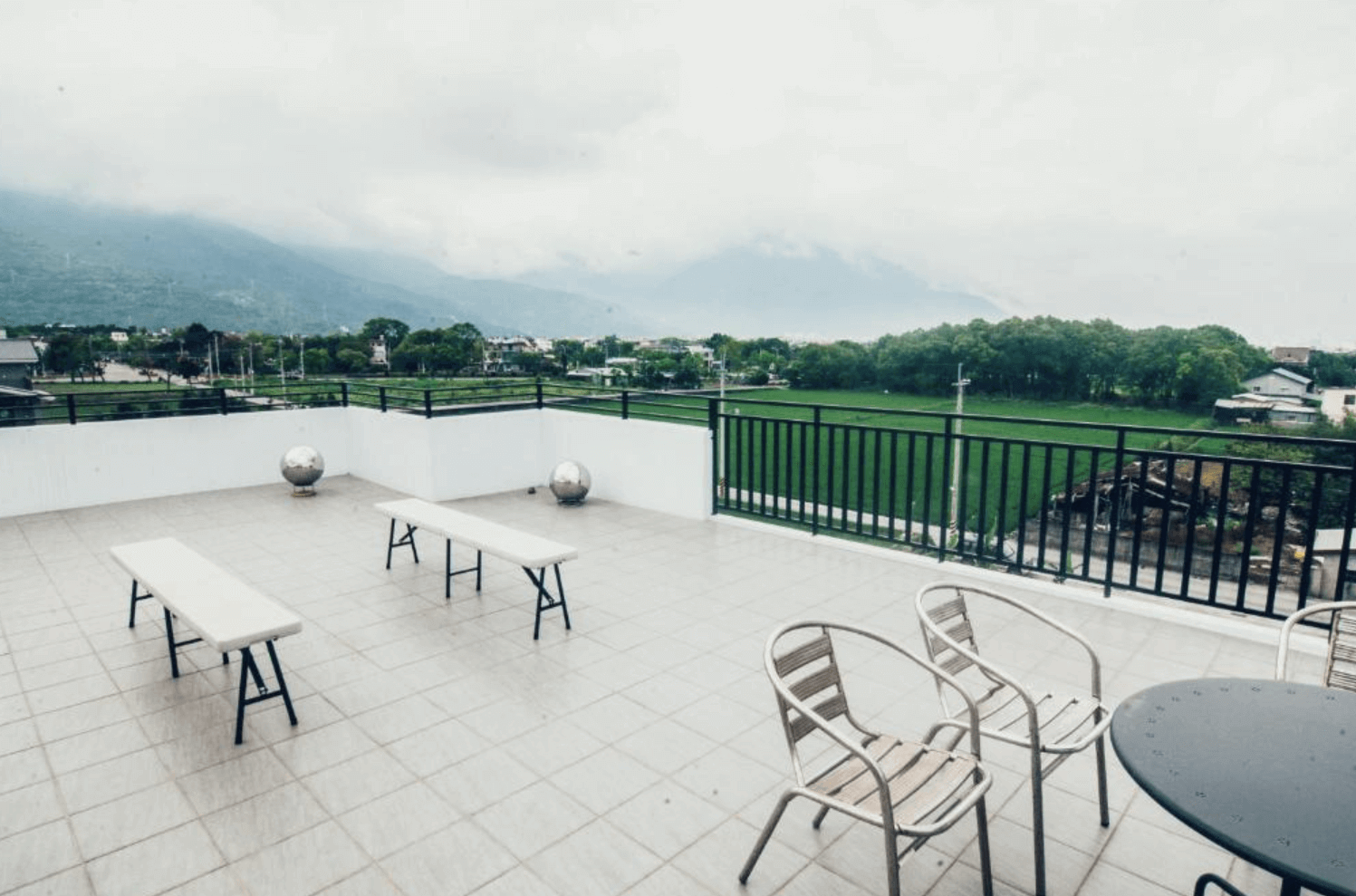 【吉安住宿】哉煙煙民宿 頂樓觀景露台，設有金屬桌椅與長凳，可遠眺綠油油稻田與遠方山脈景色，享受花蓮田園與山景的寧靜氛圍。