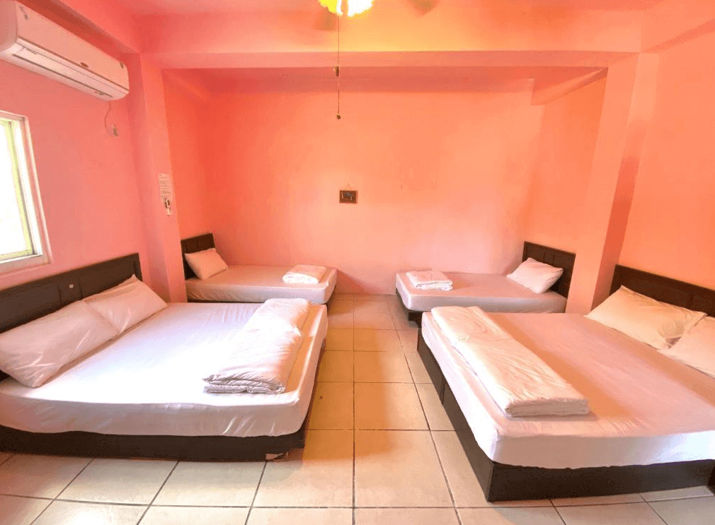 【蘭嶼住宿】嘟嘟悟的家四人房：房間粉色牆面搭配兩張雙人床與兩張單人床，簡約設計，空間寬敞，適合家庭或團體入住。