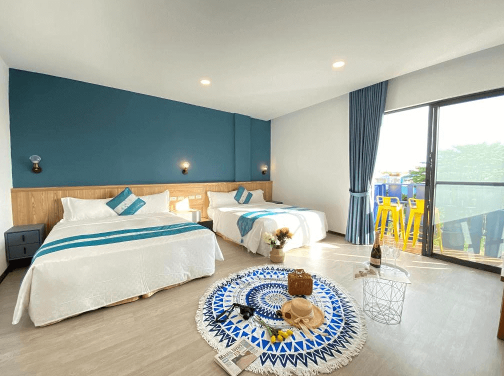 【墾丁寵物友善住宿】墾丁上好旅店家庭房 — 以藍白色調為主的寬敞房型，配置兩張雙人床，床上有藍色條紋抱枕與床旗，落地窗外設有黃色高腳椅陽台，室內擺放圓形幾何圖案地毯與小茶几。