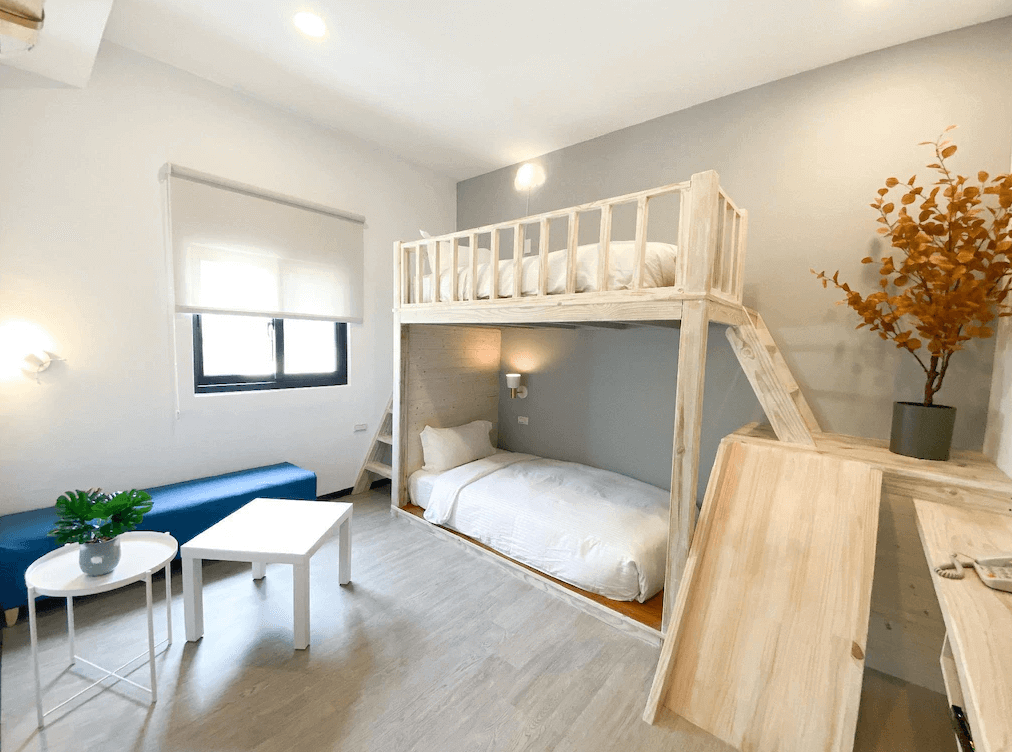 【墾丁寵物友善住宿】墾丁上好旅店上下舖房型 — 簡約明亮的房間設計，上下舖木質床架，搭配白色床鋪與灰色牆面，房內還有藍色長椅與小茶几，適合家庭或多人入住。