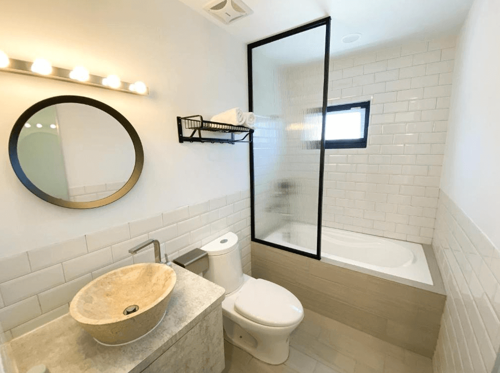 【墾丁寵物友善住宿】墾丁上好旅店浴室 — 白色地鐵磚牆搭配簡潔設計，設有浴缸與玻璃隔間，圓形鏡面與石材洗手台營造現代感。