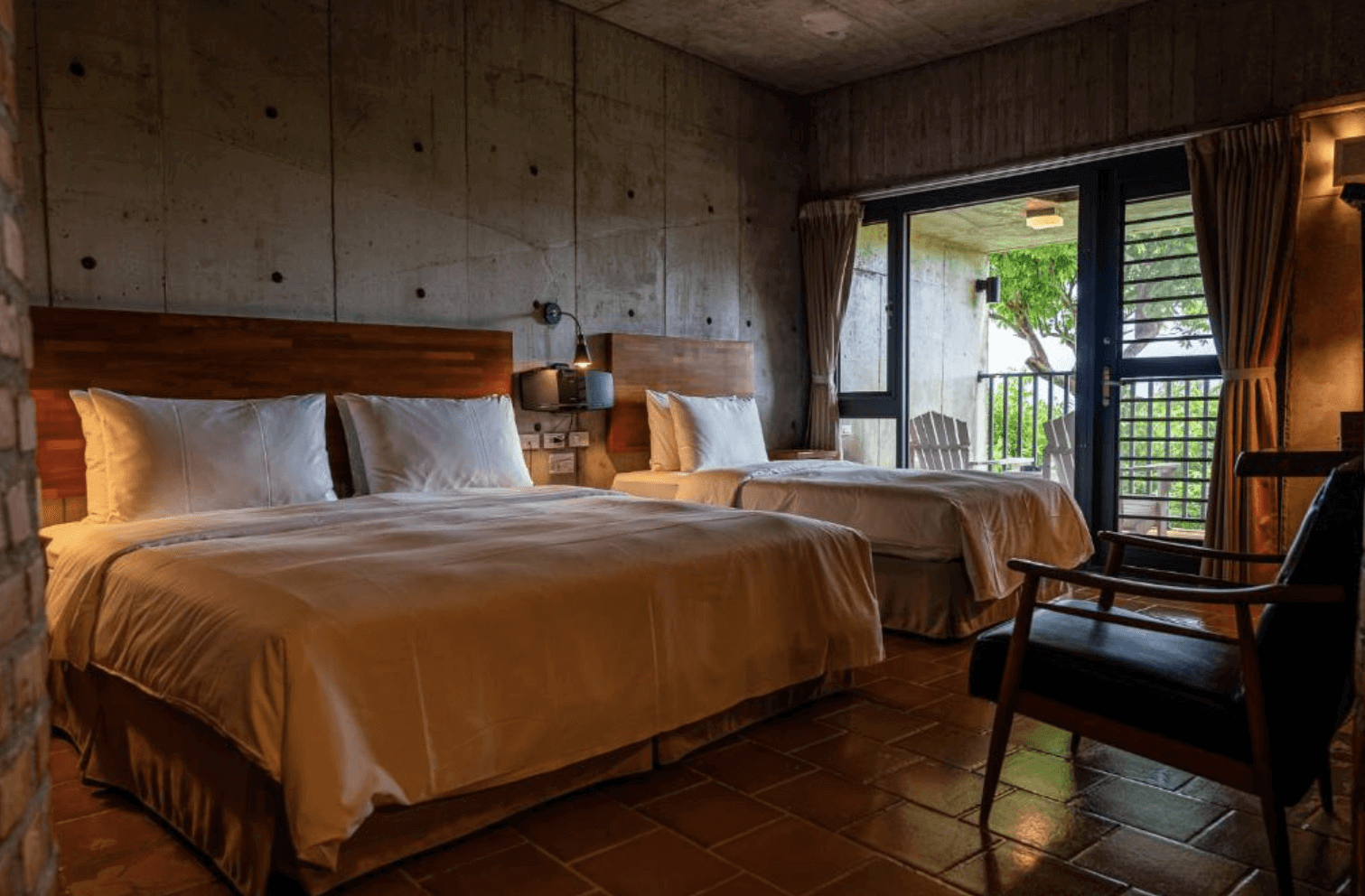 【恆春住宿】墾丁光現旅宿溫潤工業風雙床客房，混凝土清水模牆面搭配暖色照明，房內設有兩張舒適大床，連接陽台可遠眺綠意景致，充滿沈靜質感。