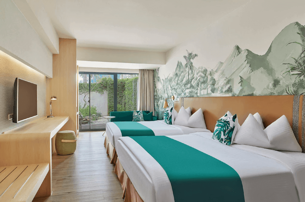 【墾丁寵物友善住宿】墾丁凱撒大飯店四人房 — 寬敞明亮的房間配置兩張雙人床，床上鋪有綠色床旗與熱帶葉子圖案抱枕，牆面有山林壁畫裝飾，窗外連通私人花園景觀