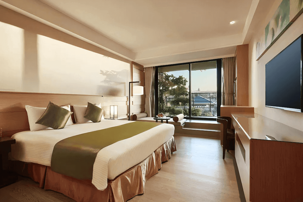 【墾丁寵物友善住宿】墾丁凱撒大飯店雙人房 — 溫潤木質風格的客房，配置一張特大雙人床與綠色床旗，大片落地窗可眺望戶外景色，並有舒適沙發區與書桌