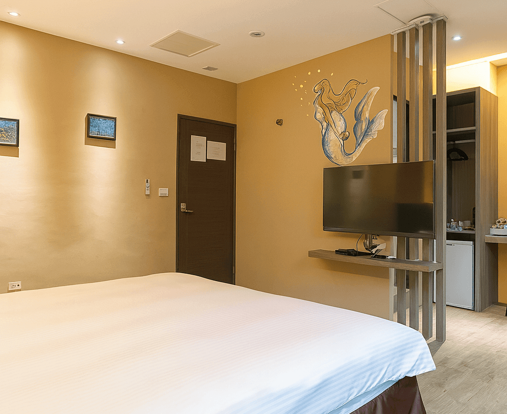 【墾丁寵物友善住宿】墾丁巴里巴里雙人房 — 溫暖米黃色牆面搭配美人魚牆繪裝飾，房內設有雙人床與壁掛式電視，旁邊有迷你吧與小冰箱。