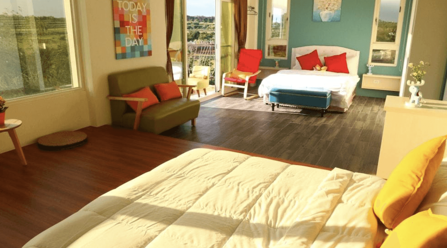 【恆春住宿】墾丁白沙灣玹玹映月民宿的家庭房空間，雙床設計搭配大片窗景，窗外為自然綠意景觀，室內有沙發、彩色抱枕與溫暖色調牆面，營造舒適又溫馨的氛圍。