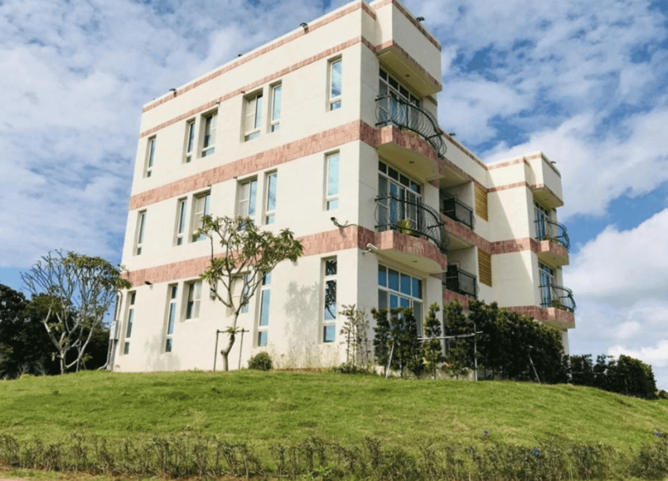 【恆春住宿】墾丁白沙灣玹玹映月民宿的建築外觀照，為三層樓高的簡約建築風格，外牆採用米白與磚紅相間設計，座落於大片綠地草皮上，周圍環境幽靜宜人。