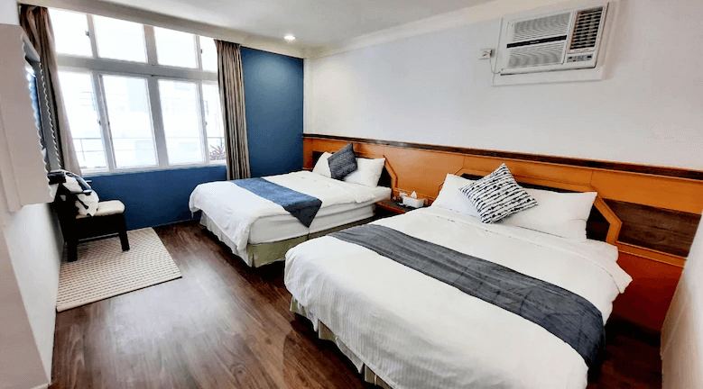 【墾丁寵物友善住宿】墾丁青山旅店雙床家庭房 — 房內設有兩張雙人床，床上搭配藍灰色床旗與抱枕，牆面以藍色與橙色木質板裝飾，採用木地板與大面窗戶，空間明亮。