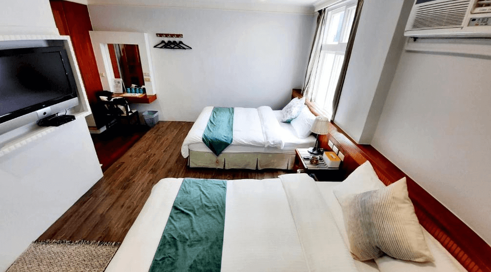 【墾丁寵物友善住宿】墾丁青山旅店雙床房 — 兩張雙人床搭配綠色床旗，房間簡潔明亮，設有電視、梳妝台與大面窗戶，採木地板設計。