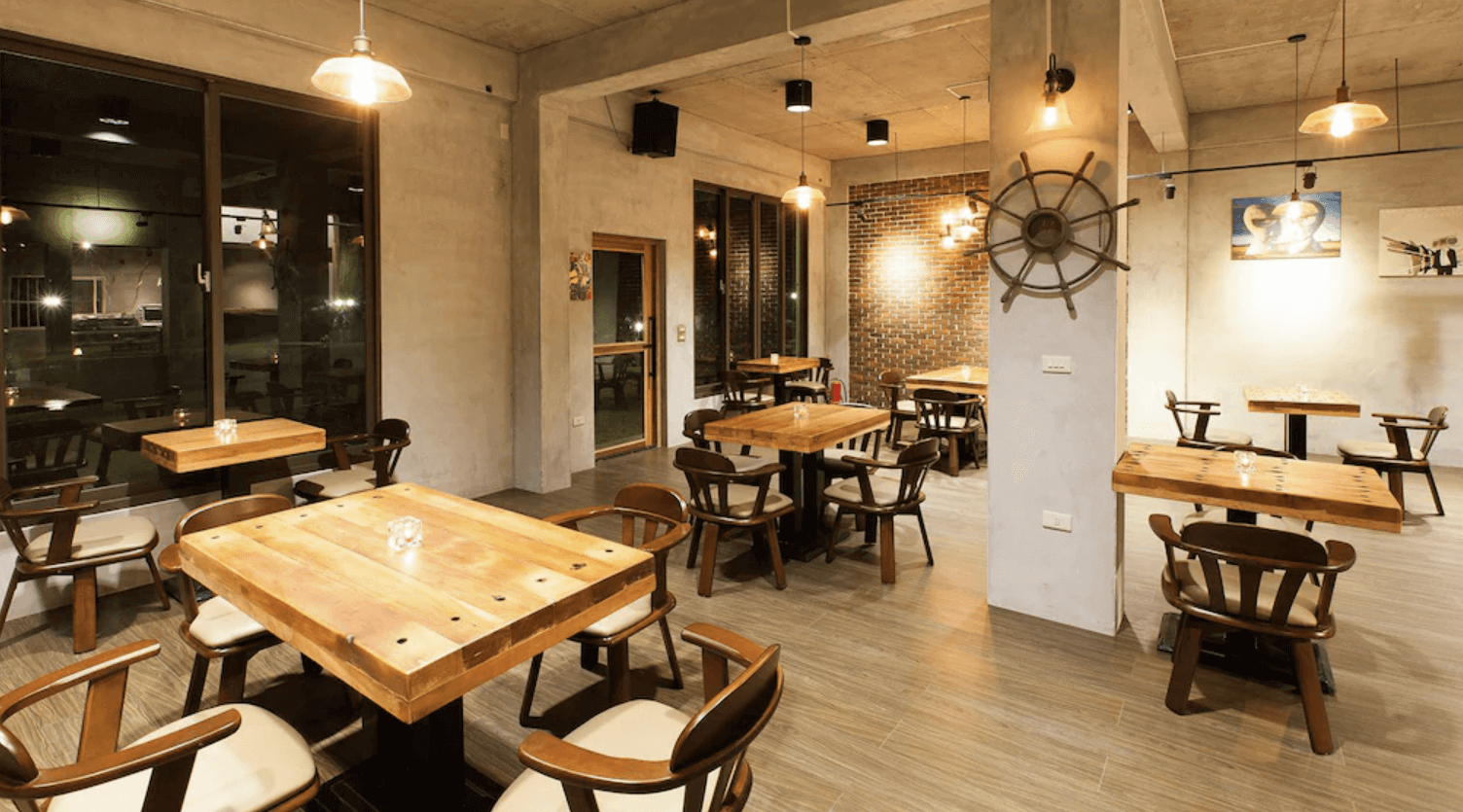 【吉安住宿】夏洛克Villa民宿 餐廳空間 — 工業風與木質桌椅結合的用餐區，大面玻璃窗採光良好，牆面裝飾船舵與藝術掛畫，氛圍溫馨。