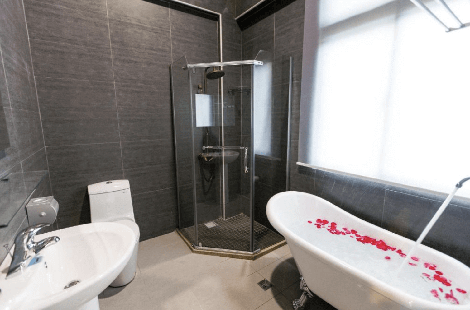 【吉安住宿】夏洛克Villa民宿 浴室空間 — 深灰色磁磚搭配獨立淋浴間與復古獨立浴缸，浴缸內鋪滿玫瑰花瓣，浪漫又放鬆。
