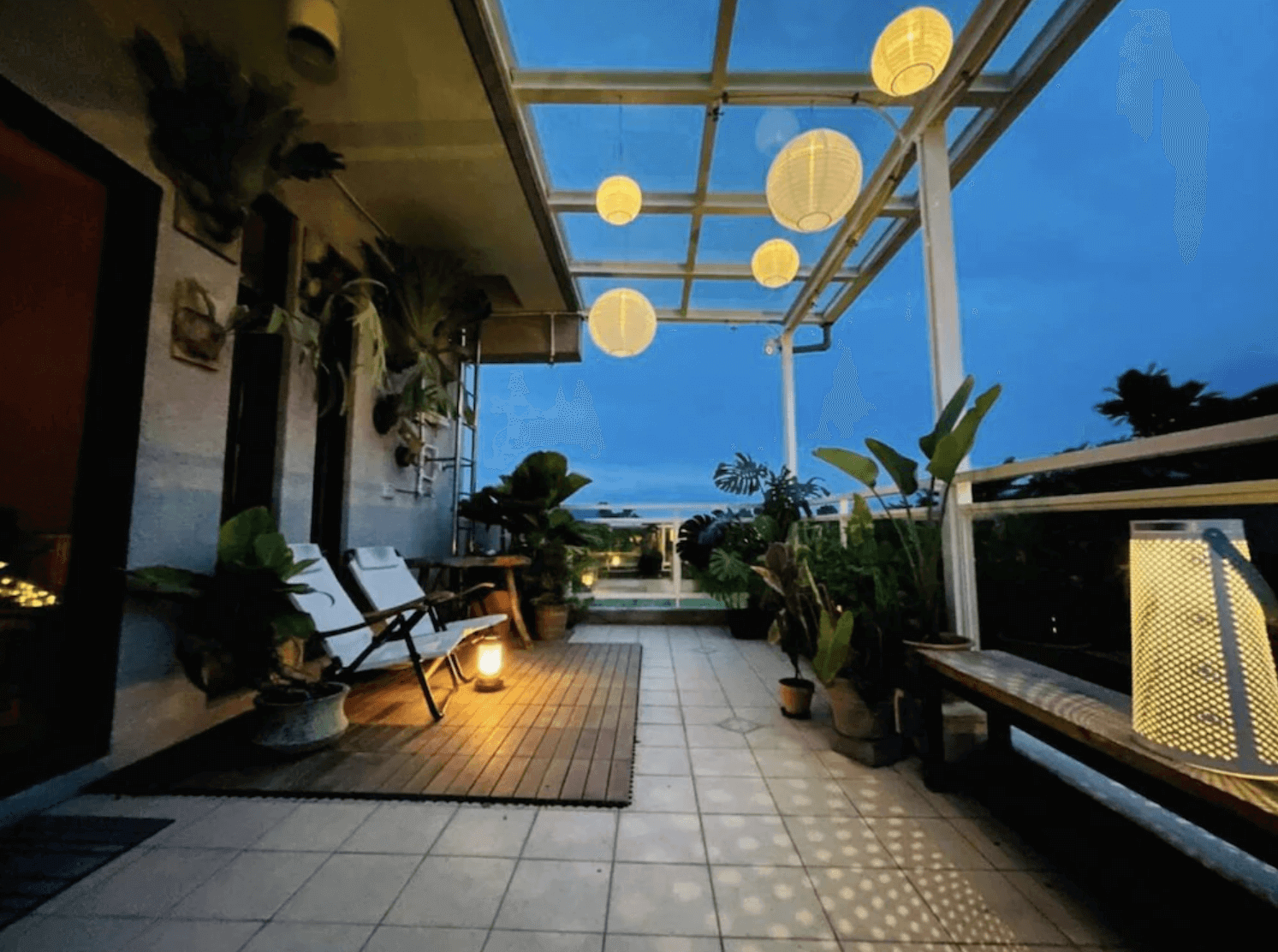 【吉安住宿】娜吉瑪民宿露天陽台夜景，鋪設木地板與磁磚，擺放白色休閒椅與植栽，懸掛暖黃色燈籠，氛圍浪漫悠閒。