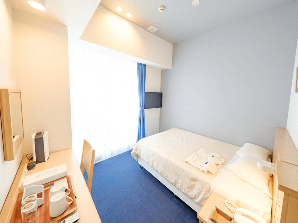 【宮古島住宿】宮古島旭日飯店的單人房設計簡潔溫馨，搭配藍色地毯與白色床鋪，提供舒適的住宿環境與基本辦公桌椅，適合獨旅或情侶入住。