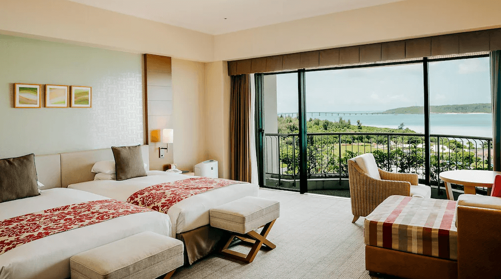 【宮古島住宿】宮古島東急飯店的雙床海景客房，房內設計溫馨典雅，大片落地窗外可遠眺伊良部大橋與碧海藍天，搭配舒適沙發與陽台空間，適合親子或雙人旅客入住。