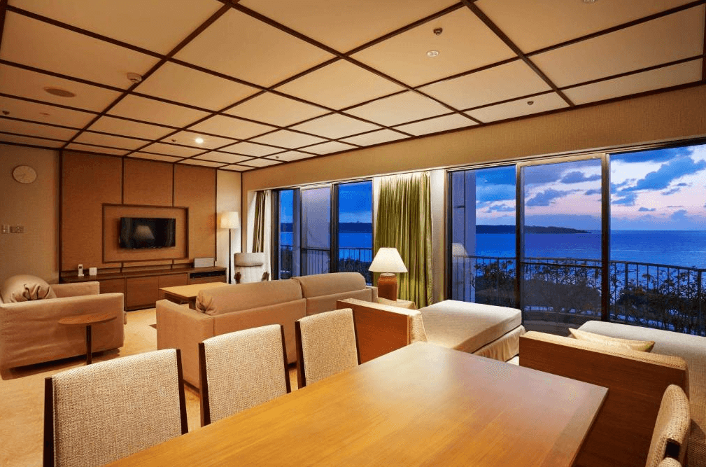 【宮古島住宿】宮古島東急飯店豪華套房的寬敞客廳空間，配有和風格天花板設計與舒適沙發，窗外可眺望夕陽海景，適合家庭或多人團體入住，享受靜謐與奢華。