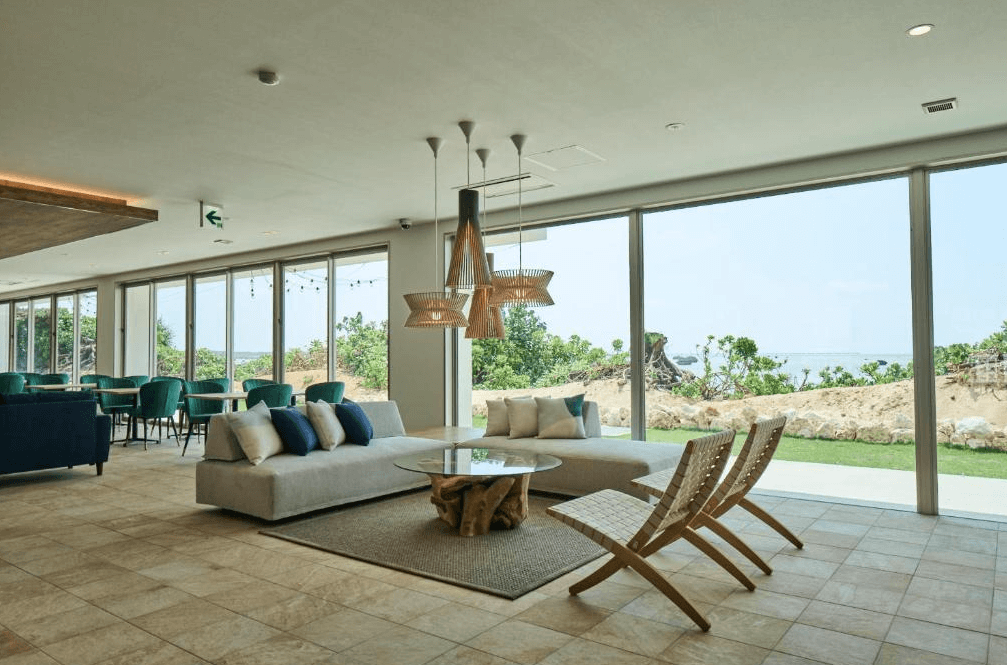 【宮古島住宿】宮古島水印飯店的大廳空間採用落地窗設計，明亮通透，配有沙發區與木質裝飾，視野可通往庭園與海岸景致，是旅客放鬆交誼的好去處。