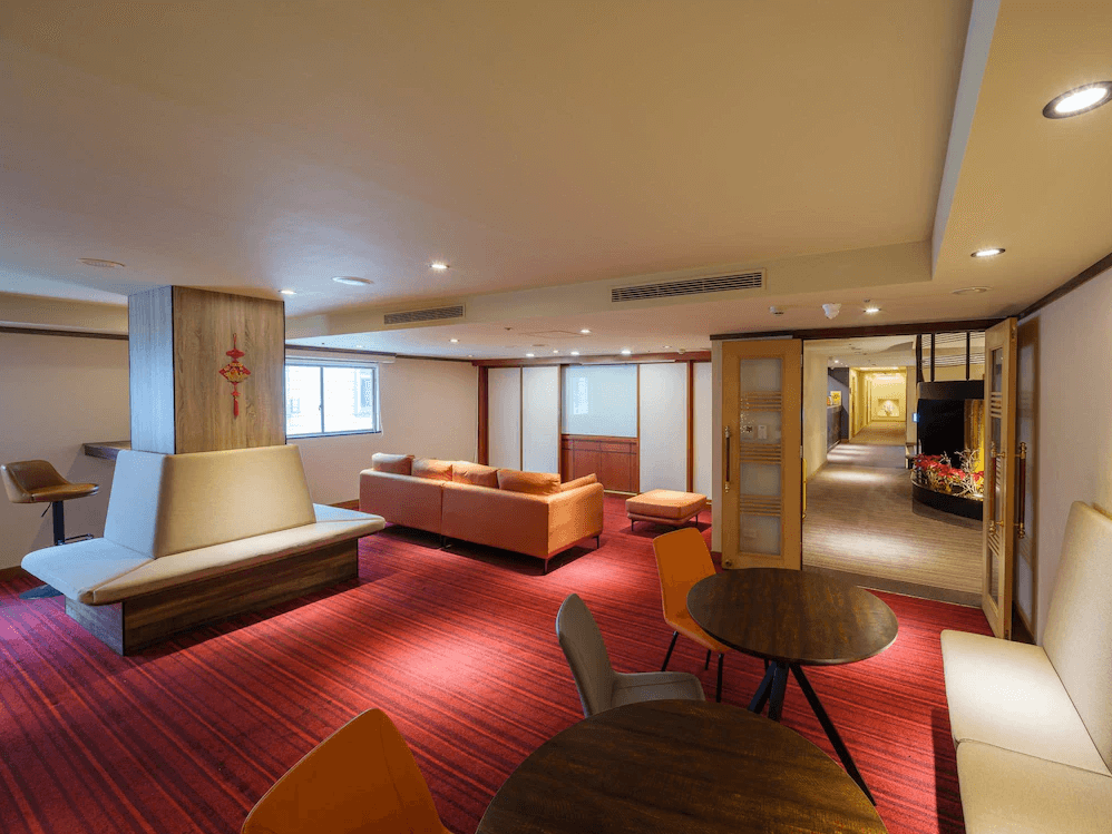 【板橋住宿】富逸旅趣-板橋府中館 公共交誼廳 – 溫馨的休憩空間，紅色地毯搭配沙發座椅與圓桌，適合旅客放鬆聊天，空間延伸至飯店走廊。