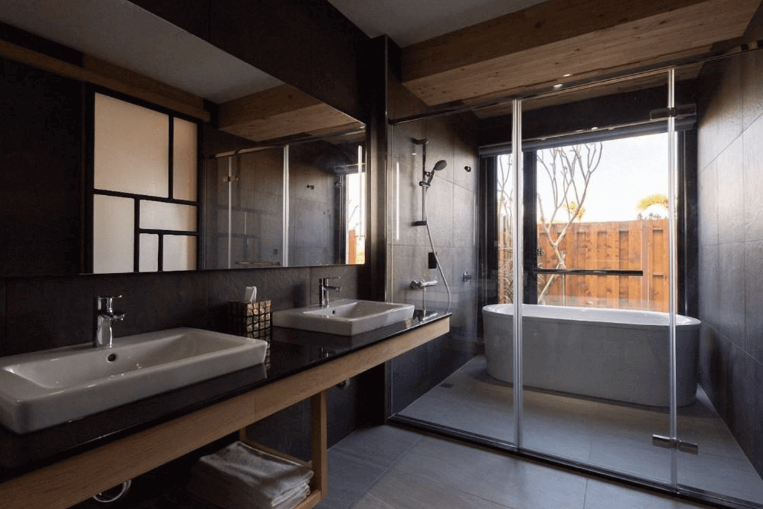 【恆春住宿】嵐翎白砂渡假莊園衛浴空間，採用現代深色磁磚設計，雙洗手台、乾濕分離淋浴間與大片窗戶旁的獨立浴缸，採光極佳，結合木質與日式簡約風格。