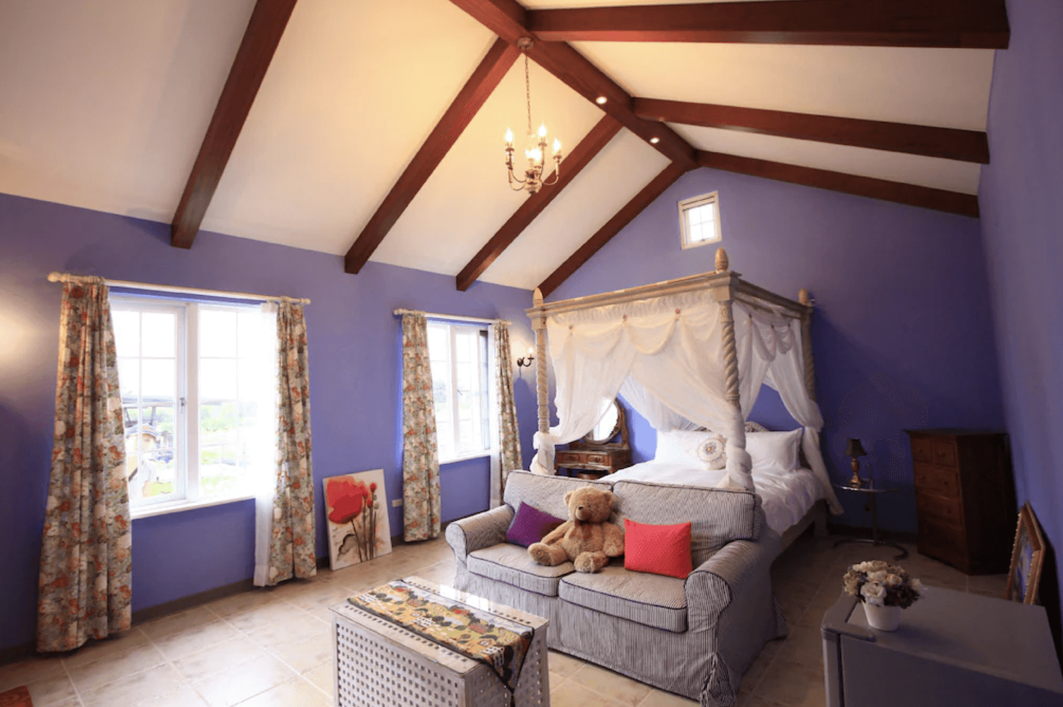 【吉安住宿】干城小鎮民宿 浪漫四柱床雙人房 — 紫色牆面與木質屋樑設計，搭配浪漫四柱床與紗簾，房內設有沙發與溫馨擺飾，採光明亮。