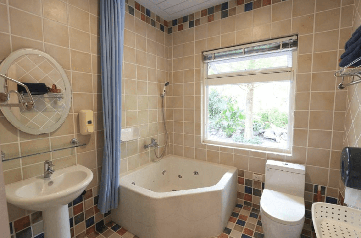 【吉安住宿】干城小鎮民宿 浴室空間 — 米色與彩色馬賽克磁磚設計，配有方形浴缸、洗手台與馬桶，窗外可見綠意景觀。