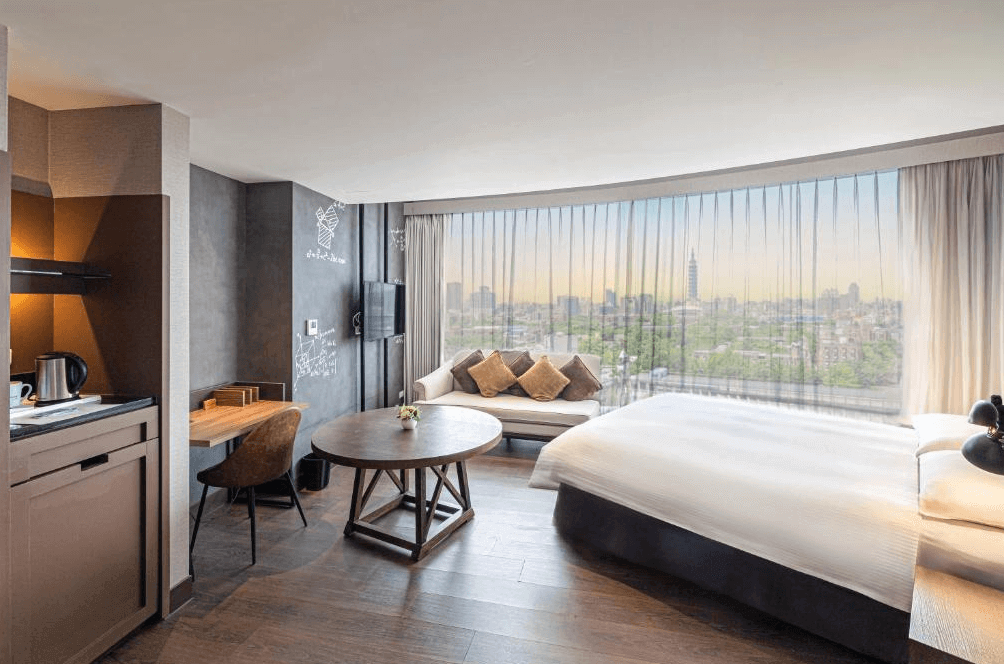 【大安住宿】捷絲旅 臺大尊賢館景觀客房 —— 寬敞的客房設有大面落地窗，可俯瞰台北101與城市景觀，內含大床、沙發、圓桌與簡易小廚房。