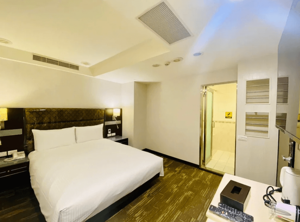 【板橋住宿】旅居文旅板橋車站館客房三：帶有暖色燈光的大床房，床頭設有皮革質感裝飾，房內配備電視、熱水壺與桌面設施，並可直通衛浴空間。