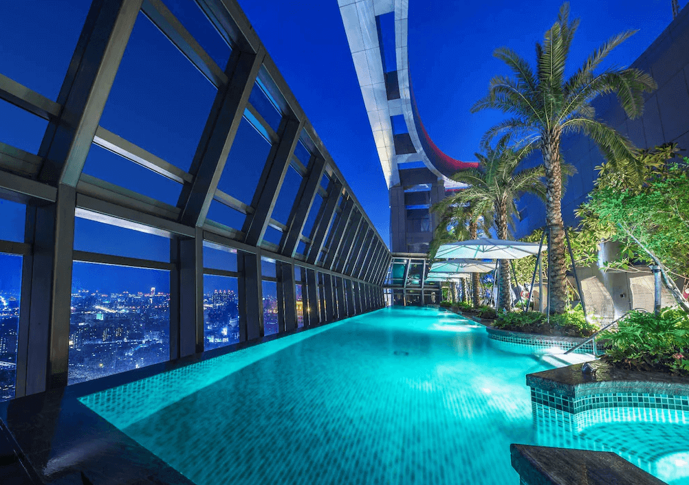 【板橋住宿】"板橋住宿精選示意圖"板橋凱撒大飯店 高空景觀泳池，夜間點燈後可俯瞰城市夜景，搭配椰子樹與植栽，展現度假氛圍。