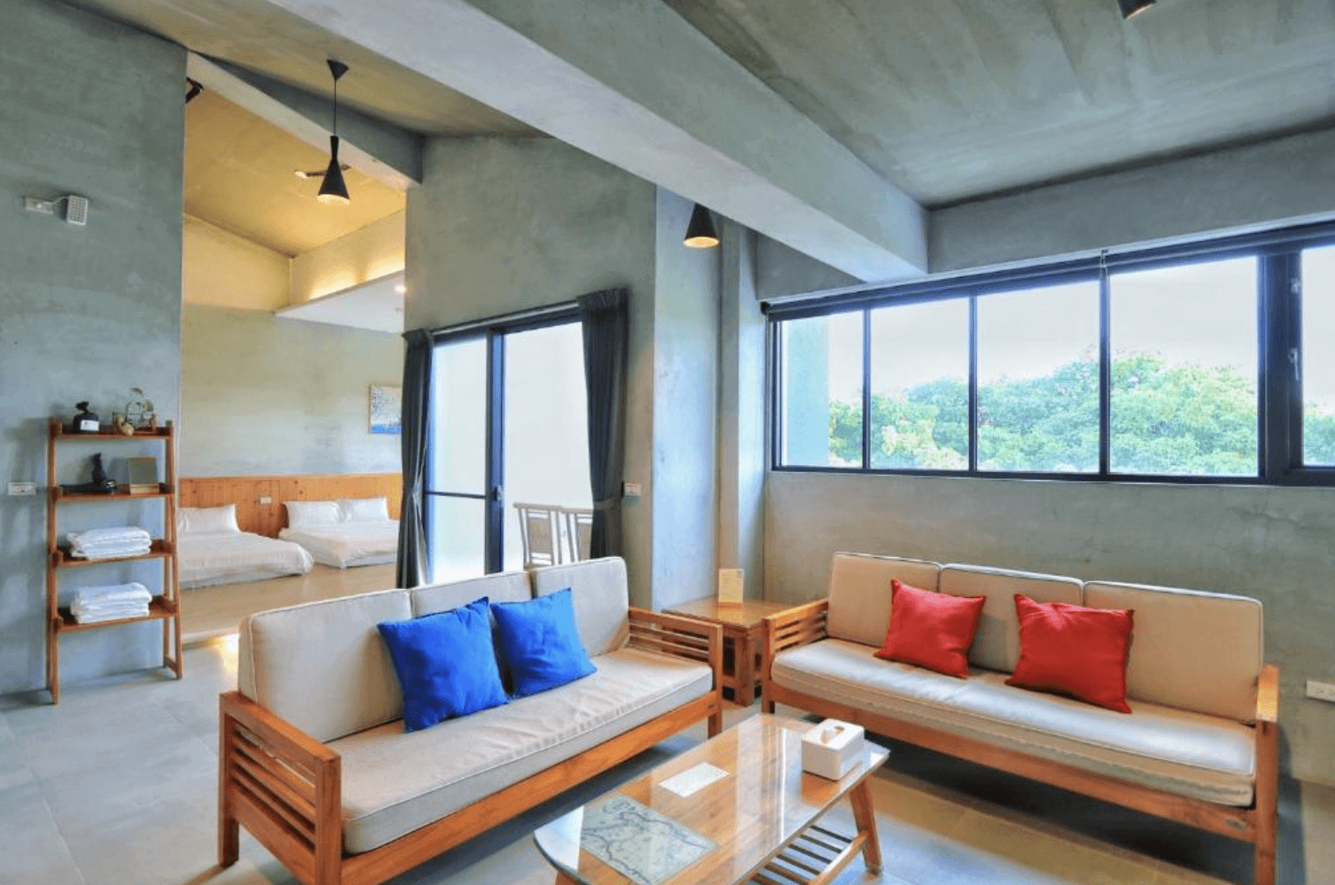 【恆春住宿】林房 Lin’s Forest 家庭房空間，採開放式設計，客廳設有木質沙發與彩色抱枕，後方為雙大床臥室，搭配大片窗景營造寧靜自在的氛圍。