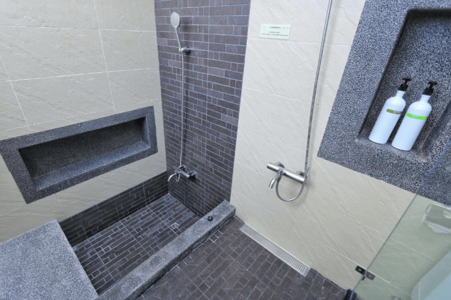 【恆春住宿】林房 Lin’s Forest 衛浴空間，採用質樸石材設計，雙蓮蓬頭乾濕分離淋浴區，牆面內嵌置物架擺放盥洗用品，展現實用與簡約美感。