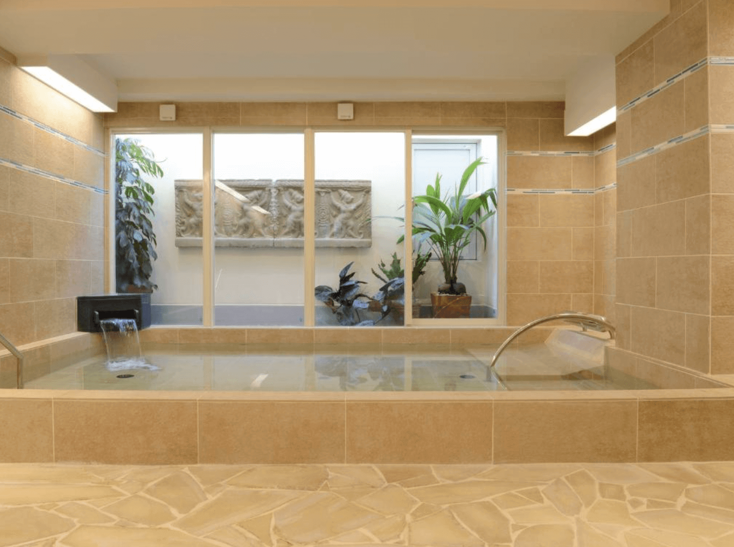 【那霸住宿】棕櫚皇家度假飯店國際通大廳 — 休憩區設有沙發與茶几，背景為接待櫃台與暖色燈光營造的溫馨氛圍。