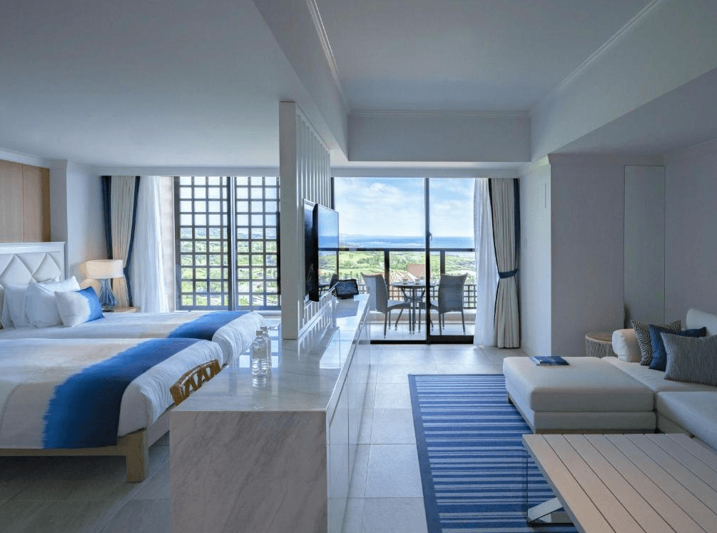 【宮古島住宿】汐姬海市飯店的海景雙人房設計以藍白色調為主，搭配沙發區與陽台座椅，營造地中海風格的度假氛圍，窗外可遠眺蔚藍海岸線。