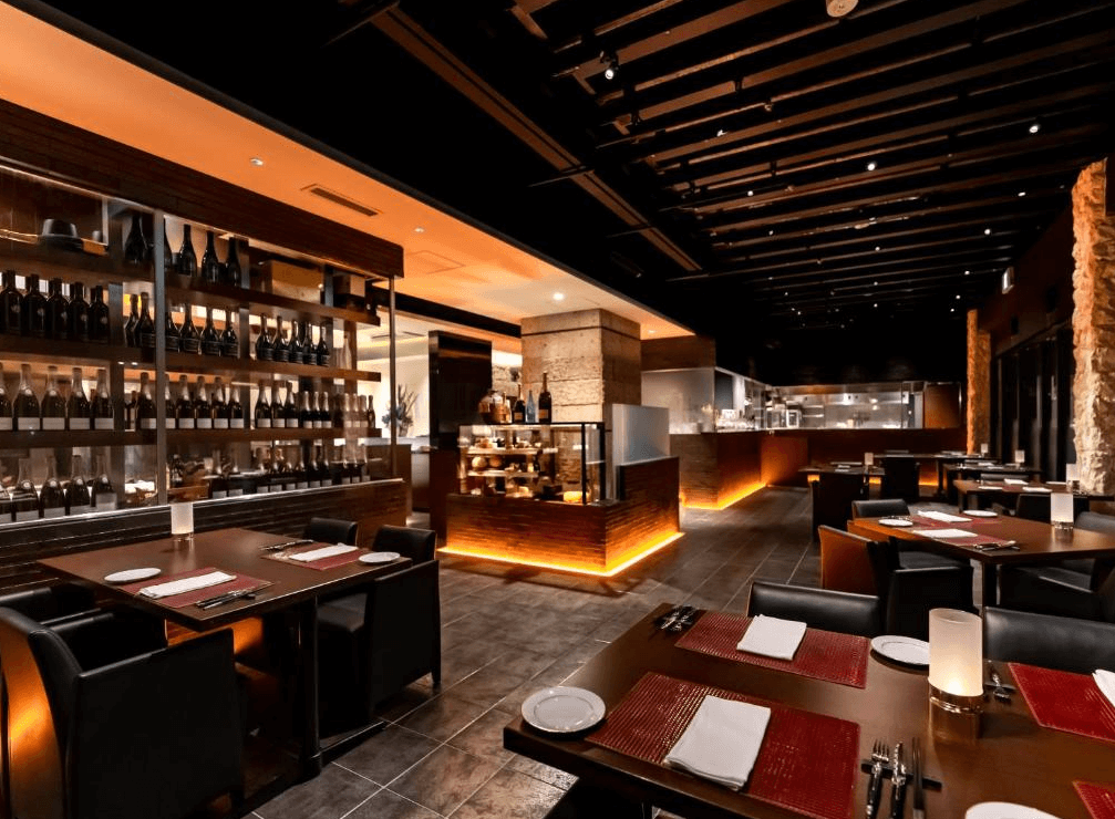 【宮古島住宿】汐姬海市飯店內的高級餐廳空間沉穩典雅，酒櫃整齊陳列紅酒與烈酒，開放式廚房與昏黃燈光打造現代奢華用餐氛圍。