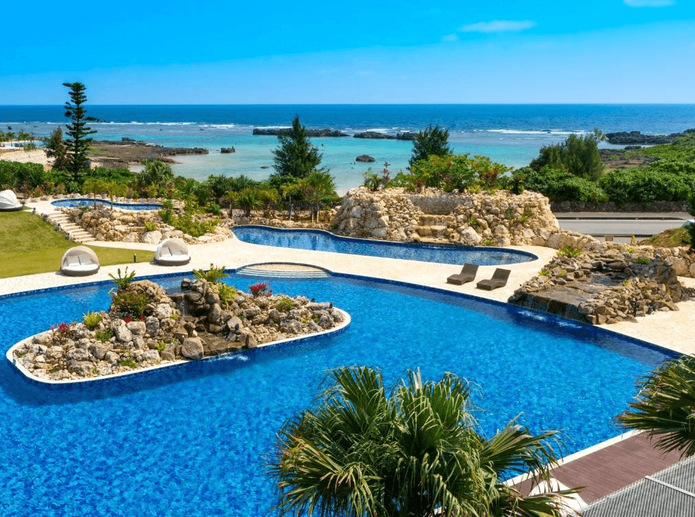 【宮古島住宿】"宮古住宿精選示意圖"汐姬海市飯店的戶外泳池區環繞著自然岩景與熱帶植物，碧藍泳池與海天一線相接，是享受陽光與戲水的絕美景點。