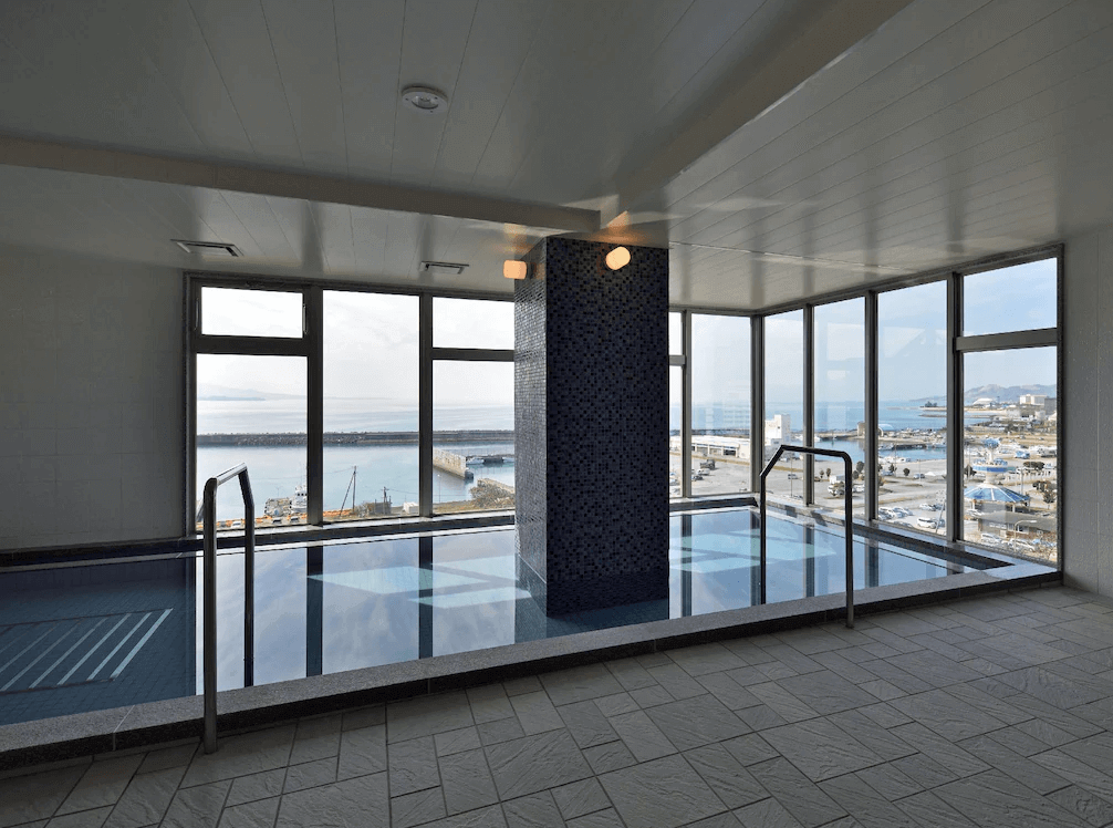 【名護住宿】沖繩名護人工溫泉二股湯之華格林里奇飯店 室內大浴場，大片落地窗可欣賞港灣與海景，設有寬敞溫泉池與休憩區，提供舒適療癒的泡湯體驗。