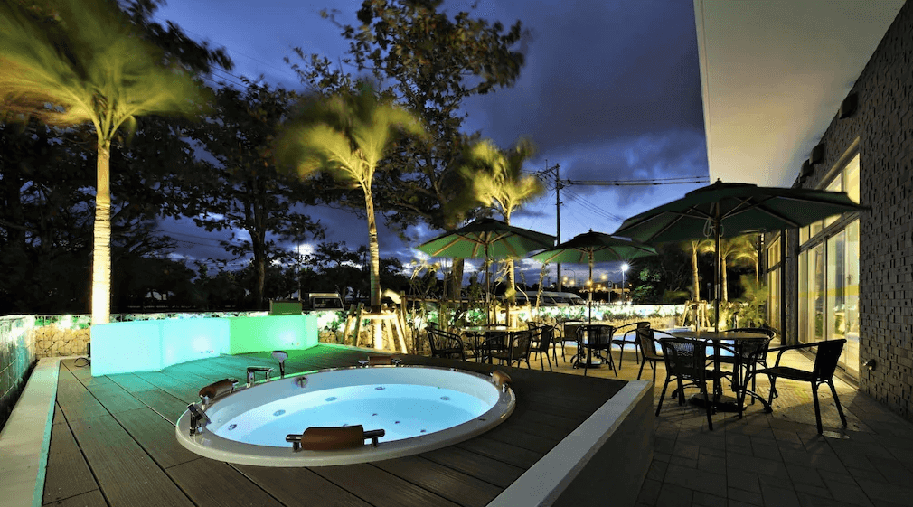 【名護住宿】沖繩名護人工溫泉二股湯之華格林里奇飯店 戶外露天按摩池，夜晚點燈搭配椰子樹與庭園座椅，營造度假氛圍，適合旅客在星空下放鬆享受。