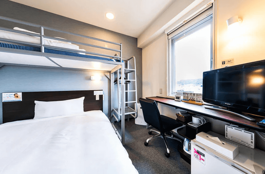 【名護住宿】沖繩名護超級酒店 (Super Hotel OKINAWA NAGO) 上下舖雙床客房，主床搭配上層單人床，房內配有書桌、電視、冰箱與辦公椅，適合親子或朋友入住。