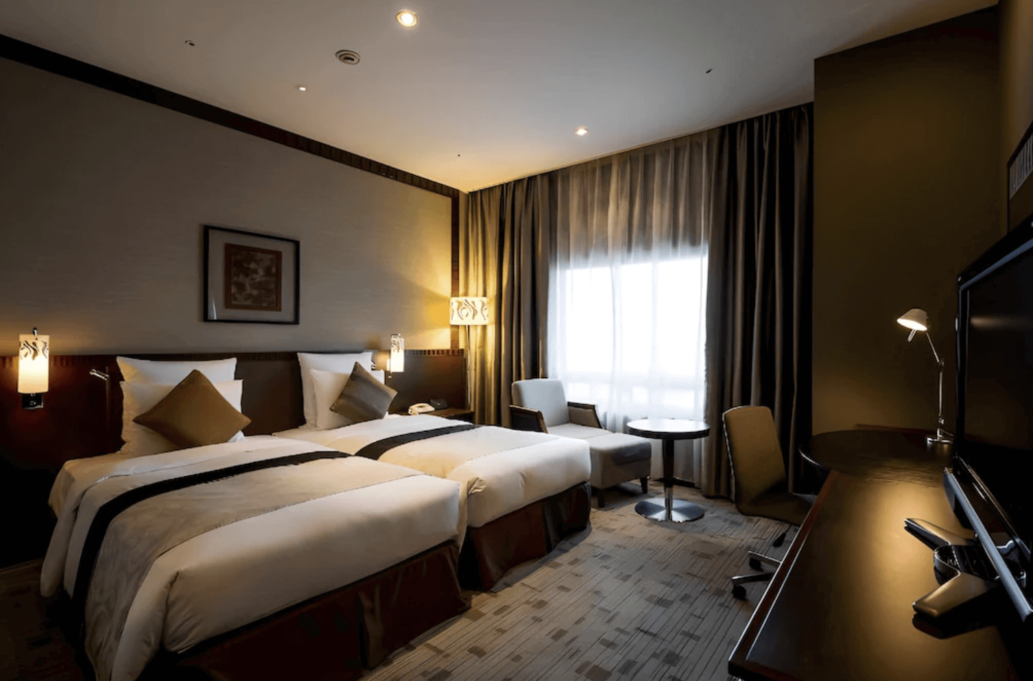 【那霸住宿】沖繩海景飯店客房 — 現代典雅的雙床房，搭配米色與棕色調設計，內設沙發與圓桌，窗外透入柔和光線。