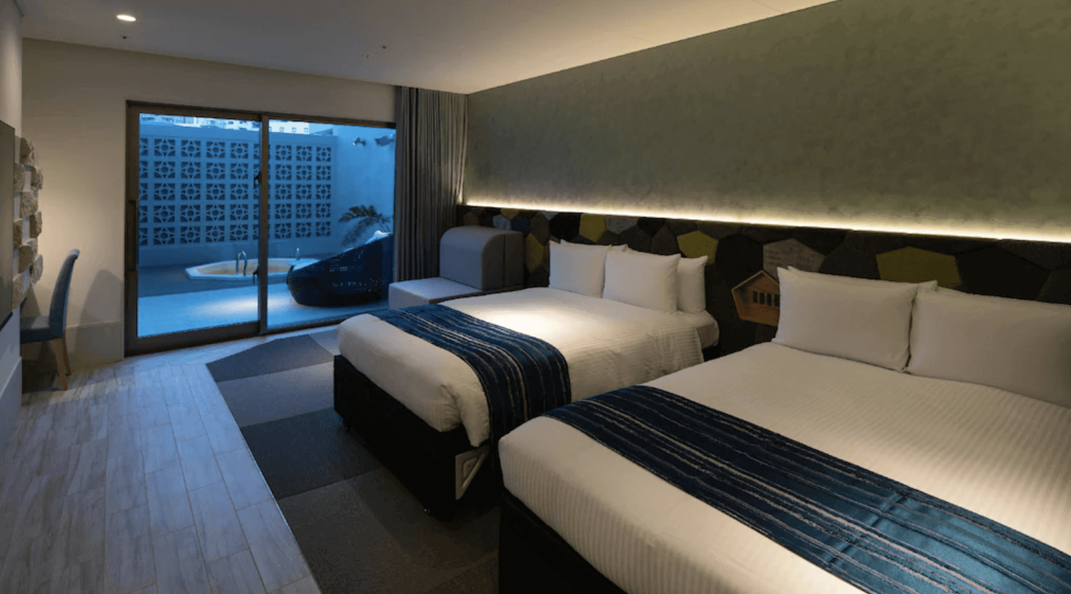 【那霸住宿】沖繩逸之彩飯店家庭客房 — 兩張雙人床搭配藍色床旗，房內設有沙發與戶外露台，可通往私人泡湯池。