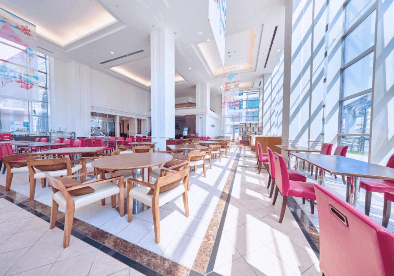 【那霸住宿】沖繩那霸美居飯店餐廳 — 挑高落地窗引入自然光，木質桌椅搭配紅色餐椅，空間寬敞明亮。