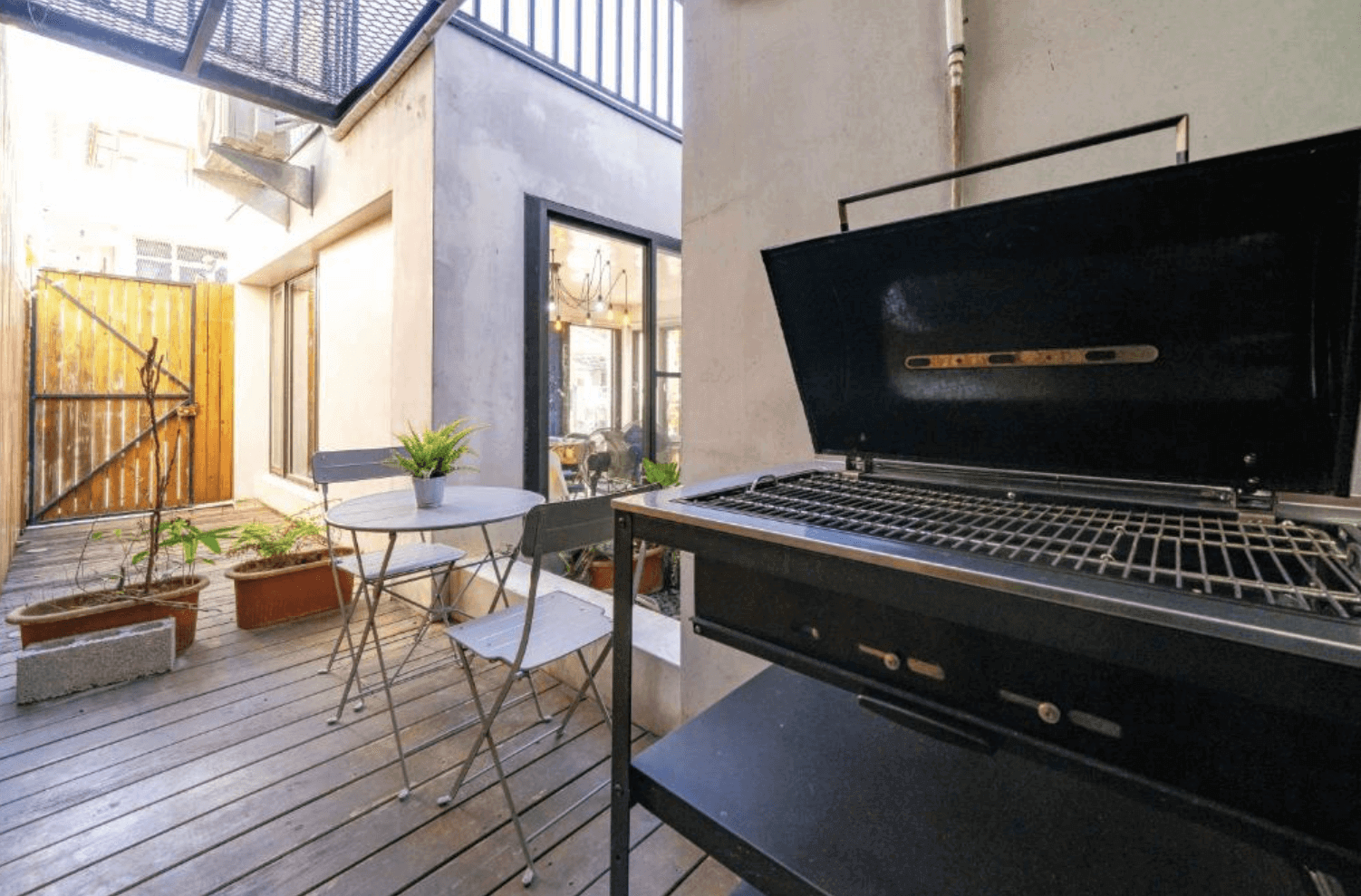 【吉安住宿】海邊很近民宿戶外露台，配置黑色烤肉爐、圓形金屬桌椅與多個花盆，木地板搭配木門圍欄。