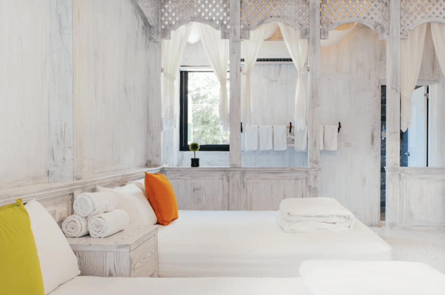 【恆春住宿】燕麥小別館房型｜純白鄉村風格雙床房，配有橘色與黃綠色抱枕、典雅鏤空窗框與白色窗簾，營造浪漫度假氛圍。