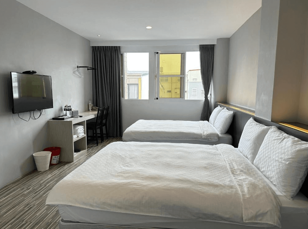 【太麻里住宿】狀元樓商務旅店雙床房型，設有書桌、電視與茶水區，灰色牆面與木質地板營造現代風格。
